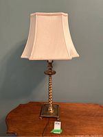 Front view of brass table lamp showing twisted rope base and beige fabric shade on wooden table against blue wall.