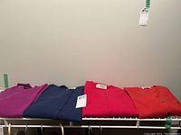 Four folded cashmere sweaters on a white wire shelf, colors purple, blue, red, and bright red, size large noted.