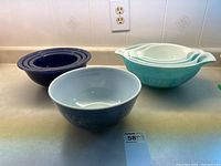 Three sets of vintage Pyrex bowls, turquoise with tiki pattern, cobalt blue nested, and a single blue floral bowl