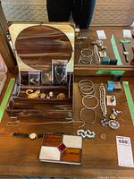 Full view of lot on wooden surface showing jewelry box with mirror, bracelets, necklaces, brooches, and stained glass box in front.