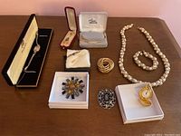 Overall view of all jewelry items including watches, pearl necklace and bracelet, cubic zirconia bracelet, brooches and pins on wooden surface