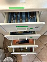 Drawers containing the flatware and kitchen utensils, showing organization in divider trays and various utensil types.