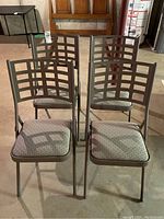Four matching metal folding chairs arranged in two rows, showing front view with padded fabric seats.