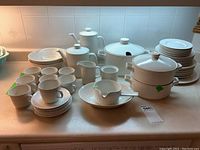 Full front view of white china set with bowls, plates, cups, teapot, coffeepot, cream, sugar, sauce boat, and covered serving bowls.