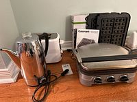 Photo showing three kitchen appliances: Sunbeam coffee percolator, Cuisinart Griddler with waffle tray accessory, Toastmaster 2-slice toaster.