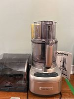 Front view of assembled Cuisinart food processor with fitted accessory container and instruction manual in background.