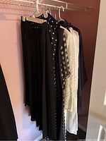 Five pieces of ladies formal clothing hanging on a rod including skirts, dresses, and pant suit jacket.