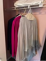 Grey blouse and skirt outfit hanging with two pink coats on hangers in closet.