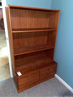 Front view of teak shelving unit, showing the four lower drawers and removable bookshelf top with two shelves.