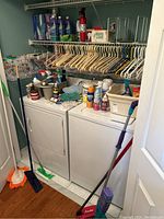 Wide angle showing full laundry room shelf and contents with hangers, cleaning products, bucket, mop handles, and machines