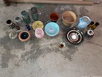 Overview of assorted pottery, planters, jars, vases, candle holders, and plates arranged on floor showing variety of materials and colors.