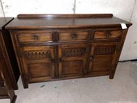 Front view of oak sideboard showing three drawers above and three cupboards below with carved detail and metal hardware.