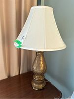 Table lamp with gold-colored pineapple-style base and cream fabric shade on wood surface.