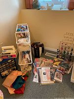 Wide view of sewing and knitting supplies including fabric, multi-drawer caddy, books, and miscellaneous items on floor