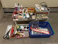 Overview of baskets and containers holding assorted sewing threads, scissors, tins of buttons, tubes of glue and other sewing supplies