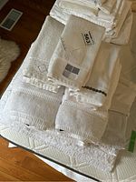 Pile of assorted white towels including bath towels, hand towels, and face cloths showing some tags and textures.