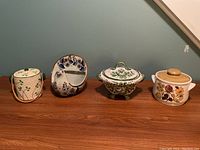 Overview of all four ceramic and pottery items on table: clover jar, blue white bird, green tureen, Sadler casserole.