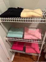 Overall view of six folded women's sweaters in different colors on wire shelves showing assortment and condition