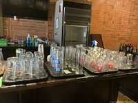 Multiple trays of assorted branded bar glasses including Guinness, Labatts 50, Steam Whistle, Bud Light, Michelob, Madri, and Mackinnon on a bar counter with brick wall background.
