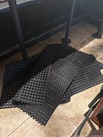 Five black rubber mats stacked on tiled floor under bar counter