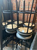 Cluster of black metal frame bar stools stacked in an upside-down position showing the bottoms of the vinyl seats and round bases.