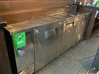 Full view of three-door stainless steel underbar fridge against wood wall