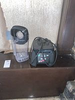 Waring commercial blender base with power cord and separate clear pitcher with black lid shown side by side on wooden surface.