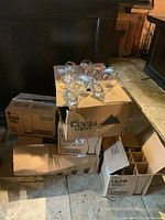 Photo showing multiple boxes stacked containing branded beer glasses, some glasses resting on boxes including Coors Light and Blue Moon logos visible.