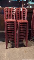 Stack of several red plastic chairs showing the front with slatted backs and seat contours.