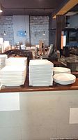 Stacks of white square plates and round soup bowls on a bar counter