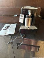 Front view of the Nespresso Cappuccinatore CS 20 coffee machine with attached frother and instruction manual beside it.