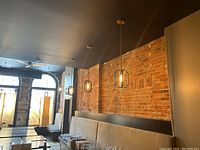 View of multiple pendant lights hanging from the ceiling above a seating area with exposed brick walls.