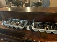 Overview of plastic utensil trays filled with various cutlery and four glass candle holders to the left.