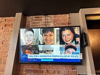 Full view of the Haier 50-inch TV mounted on a brick wall showing a news broadcast and remote control mounted next to it.