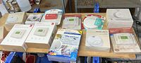 Photo showing multiple boxed items including smoke alarms, thermostats, and detectors arranged on a table.