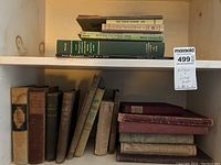 Shelf with a variety of antique books including a green book with gold lettering and several smaller vintage books stacked in two rows.