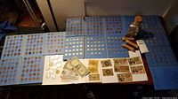 Overview of coin albums, loose coins, paper currency, coin rolls and jar on table