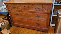 Front view of antique oak dresser showing three drawers and metal handles on wooden floor with some surrounding items.