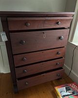 Front view of antique tallboy dresser with five wooden knob drawers, middle drawer partially open showing keyhole and key hanging from rope.