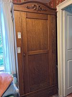 Front full view of antique tiger oak wardrobe cabinet showing carved top, single door front, and drawer base