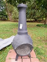 Full front view of black cast aluminum chimenea standing on brick pavers with gray cover folded beside it