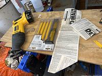 Yellow and black DeWalt cordless reciprocating saw with attached battery, user manuals and paperwork on wood surface in garage.