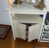 Front view of white wooden end table with top flat surface, open shelf below, and double door cabinet open showing storage space and some items inside.