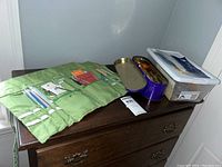 View of entire lot showing green knitting needle case, metal tin, and plastic container on wooden dresser.