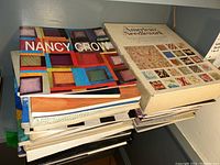 Stack of various needlework and quilting books including Nancy Crow quilt book and American Needlework book.