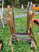 Photo showing one of the vintage organ dollies with wooden side frames, metal crossbars, caster wheels, and attached securing straps. Weathered condition visible.