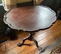 Full view of the antique wooden table showing pie crust scalloped edge and claw foot base, with visible scuffs on the surface.