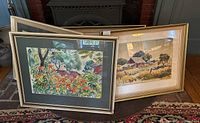 Two framed watercolors leaning against fireplace: silver frame with green mat, gold frame with white mat