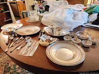 Overhead view of sterling silver platters, servers, cups, utensils and bowls arrayed on table