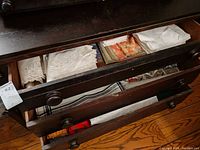 Drawer containing stacks of folded embroidered white linens, colorful printed placemats, and plain white linens